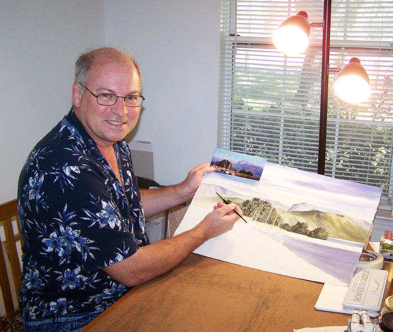 Bill Holkham painting a landscape watercolor at his desk